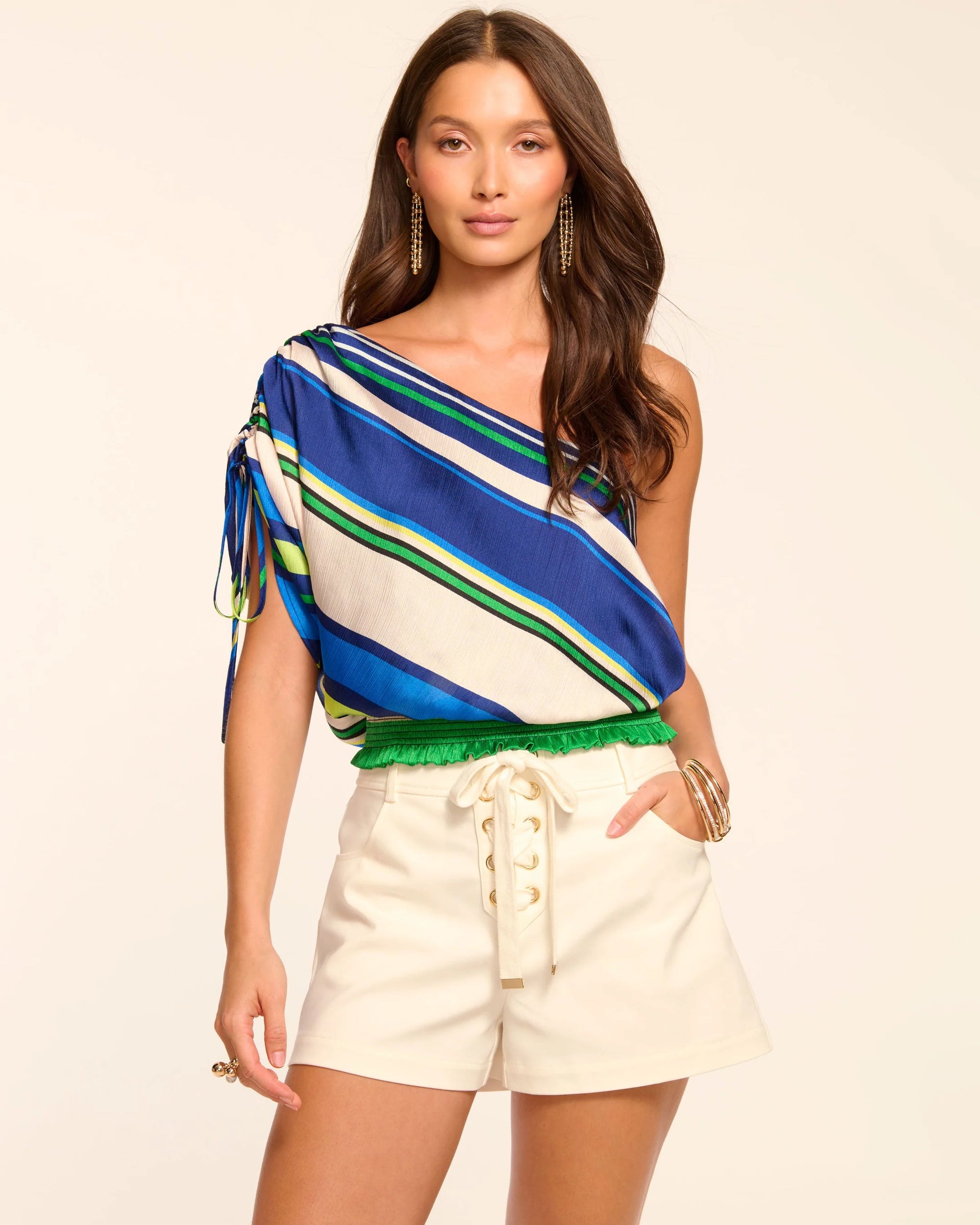 Woman wearing a colorful striped top and white shorts on a beige background