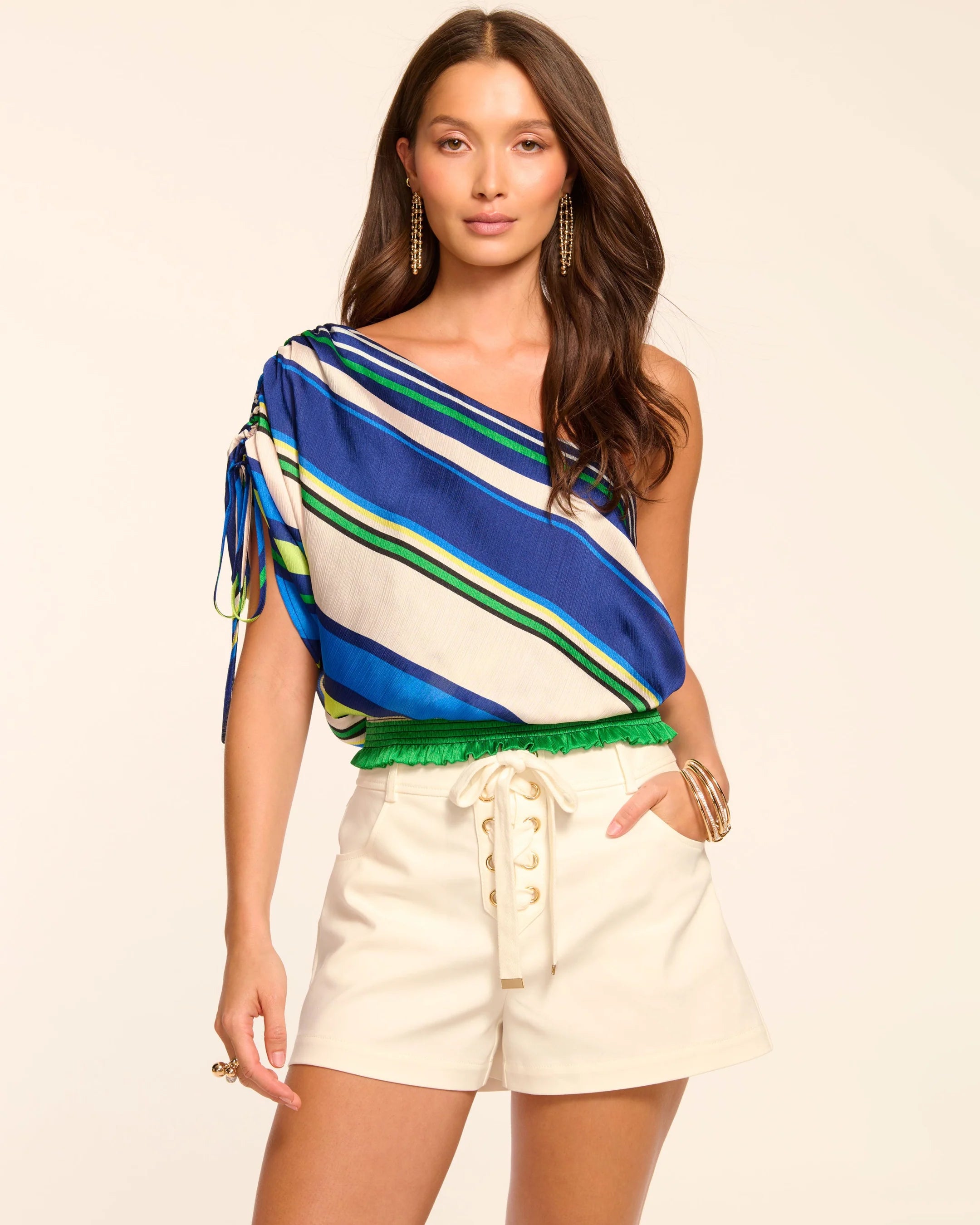 Woman wearing a colorful striped top and white shorts on a beige background